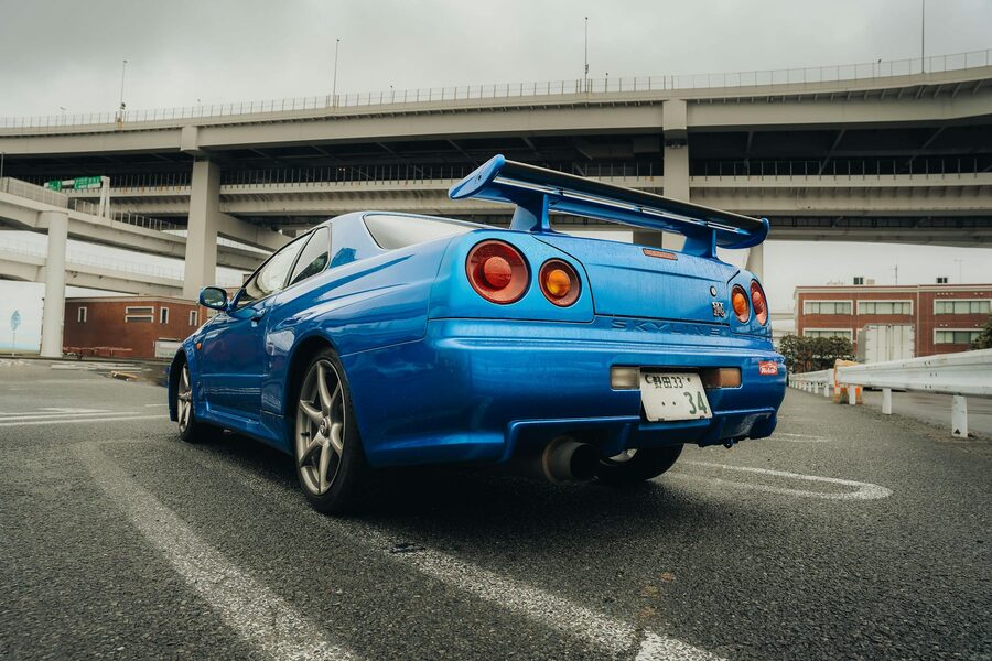 Blue Nissan R34 Skyline GTR parked beneath a concrete overpass