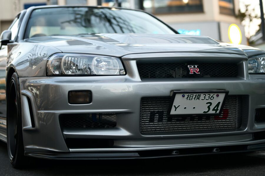 Silver Nissan Skyline R34 GTR parked on a Tokyo street with neon lights