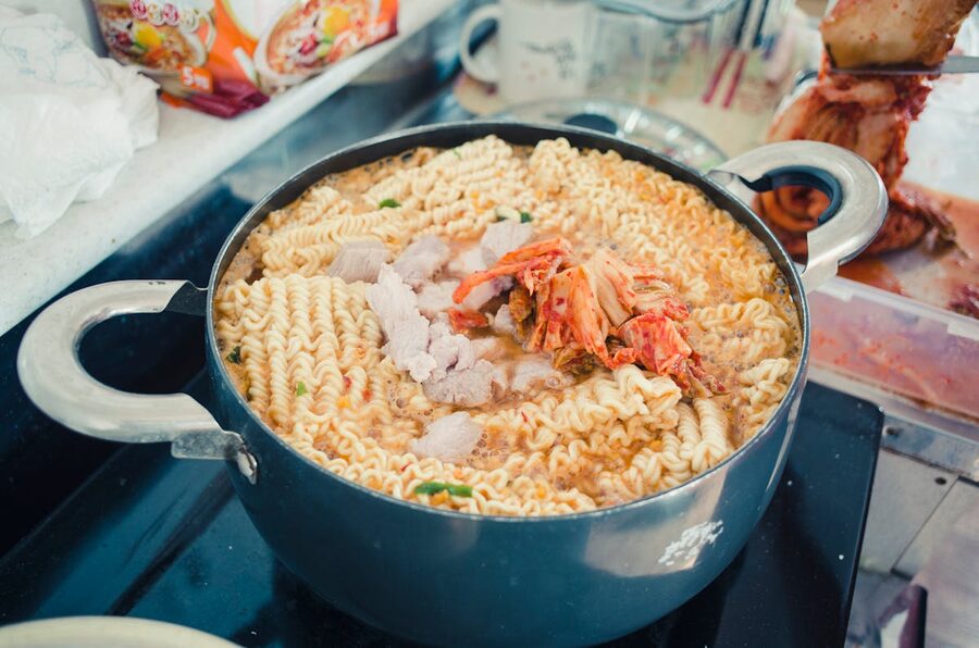 Noodles simmering in a pot of broth with vegetables visible through the steam