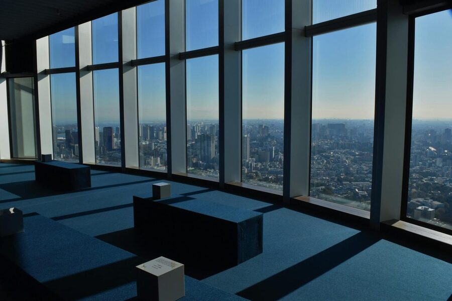 Panoramic view of Tokyo from an indoor observation deck with visitors looking out at the city