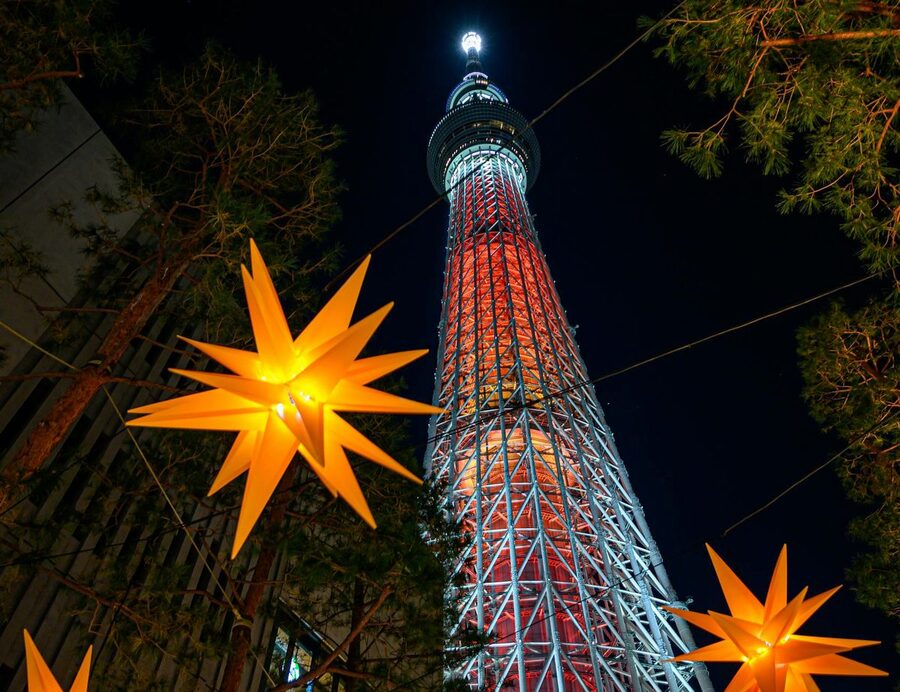 Tokyo Skytree tower glowing with colorful lights at night reflected in Sumida river
