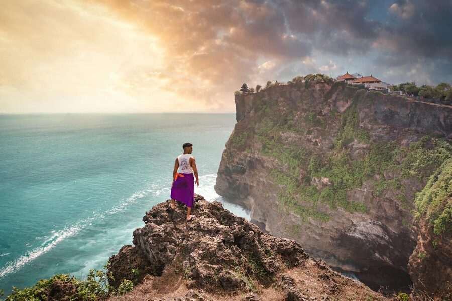 Man standing on cliff overlooking Uluwatu Temple at sunset