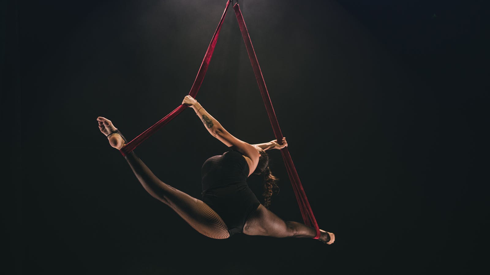 Aerial acrobat performing split on silk ribbons in dramatic lighting