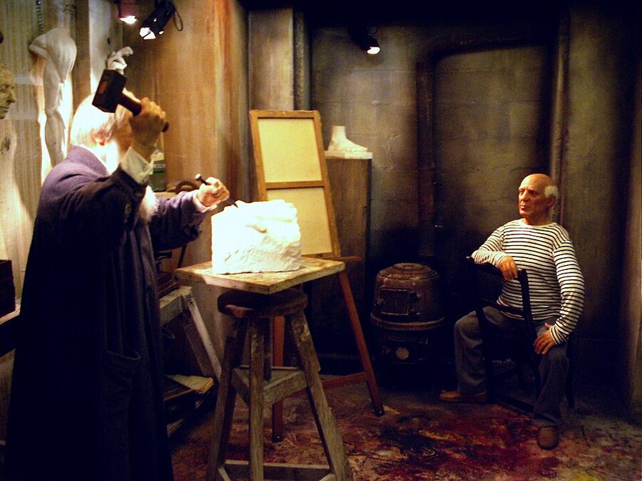 Picasso wax figure seated in striped shirt with sculptor scene at Musee Grevin