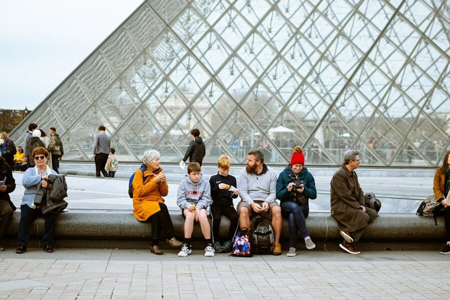 Visitors sitting near the Louvre Pyramid Paris