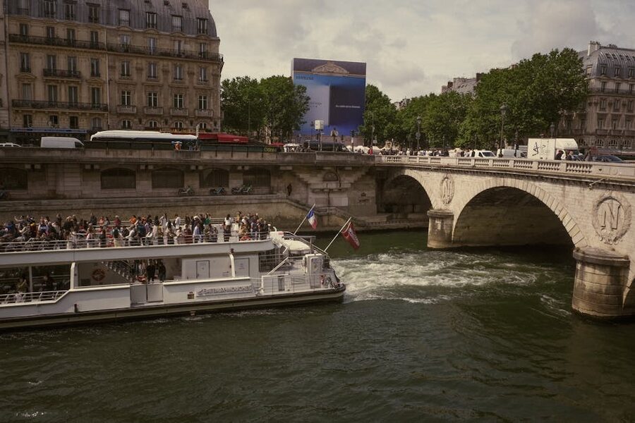 A populated Seine cruise boat passing under a Paris bridge in daytime