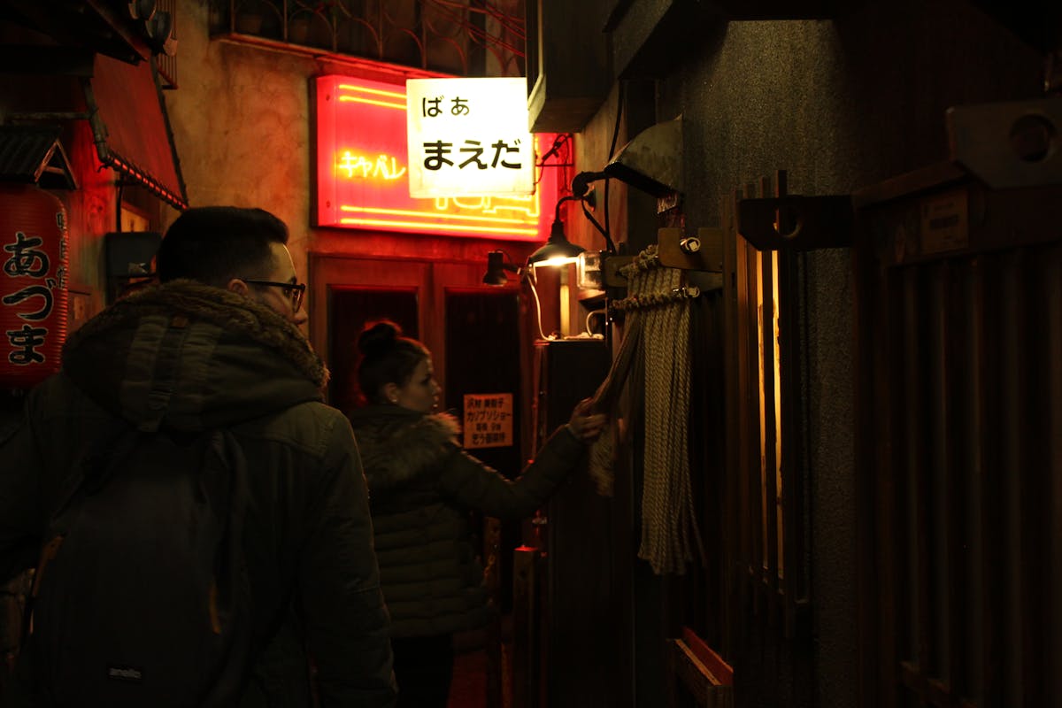 People entering a narrow neon-lit alley in Tokyo at night