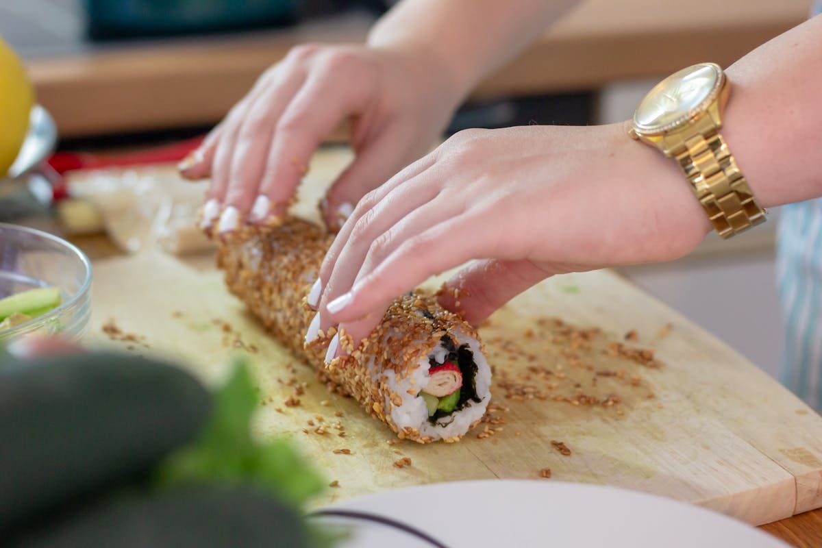 Close-up of hands rolling sushi covered in sesame seeds on a bamboo mat
