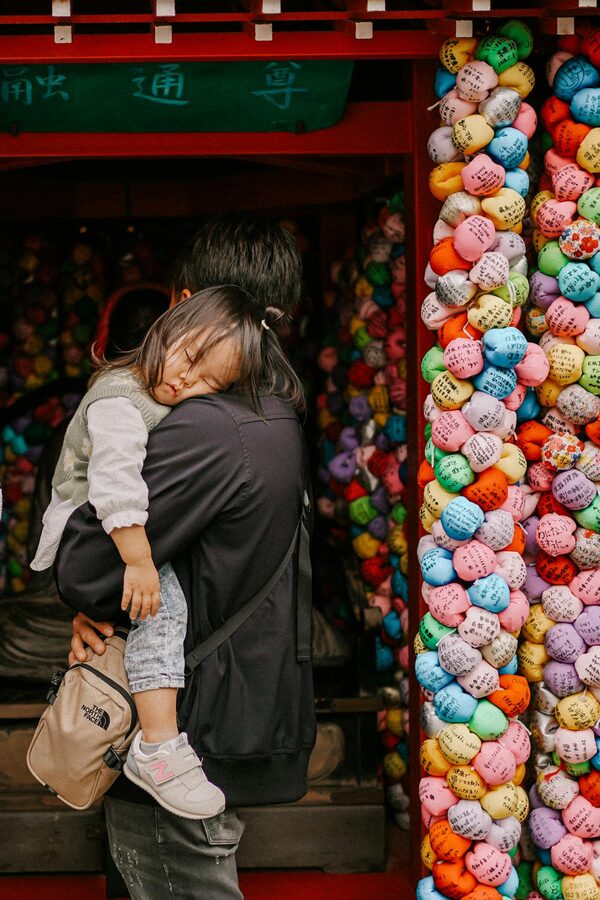 A father carries his sleeping child at a colorful Japanese temple adorned with paper lanterns