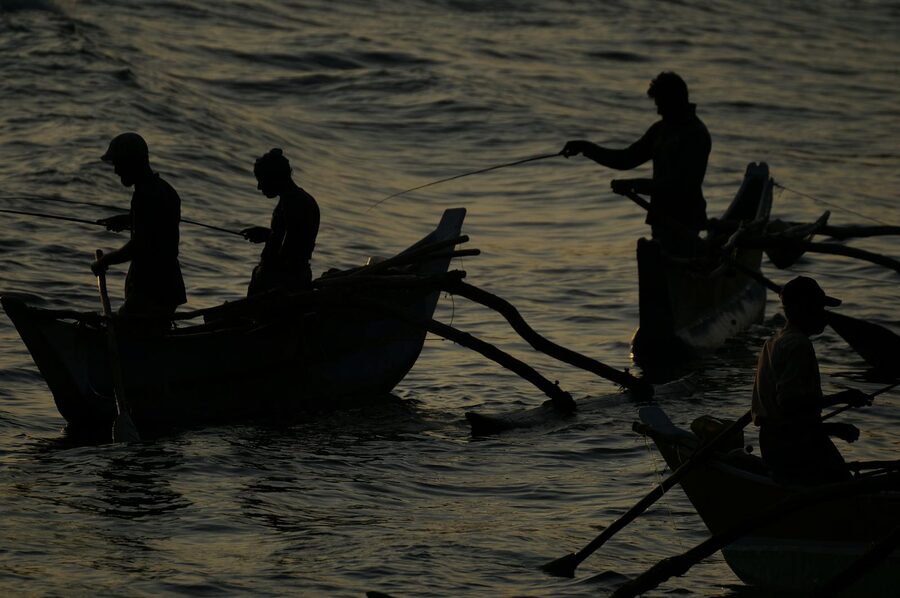Silhouettes of fishermen rowing traditional boats at sunrise on the south coast of Sri Lanka