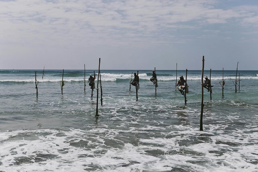 Traditional stilt fishermen perched over ocean waves on the south coast of Sri Lanka