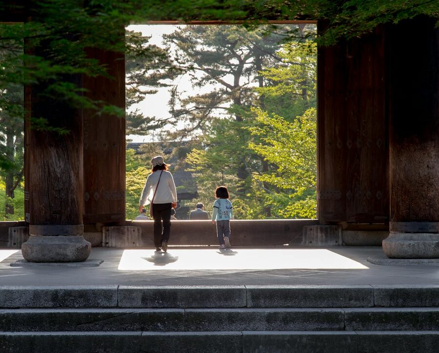 A family strolls through a temple gate surrounded by lush greenery in Kyoto Japan