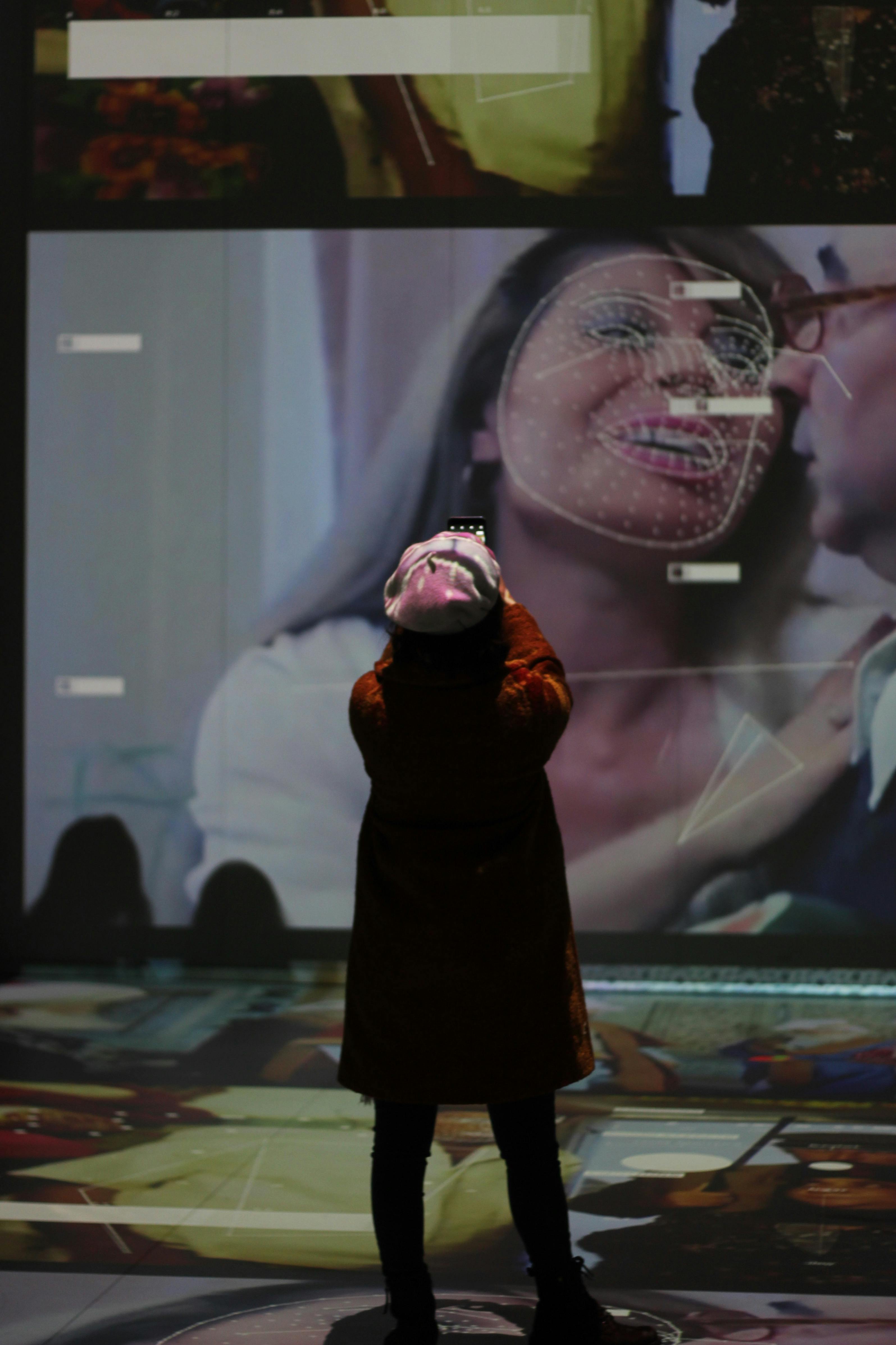 Person photographing digital art projection at exhibition