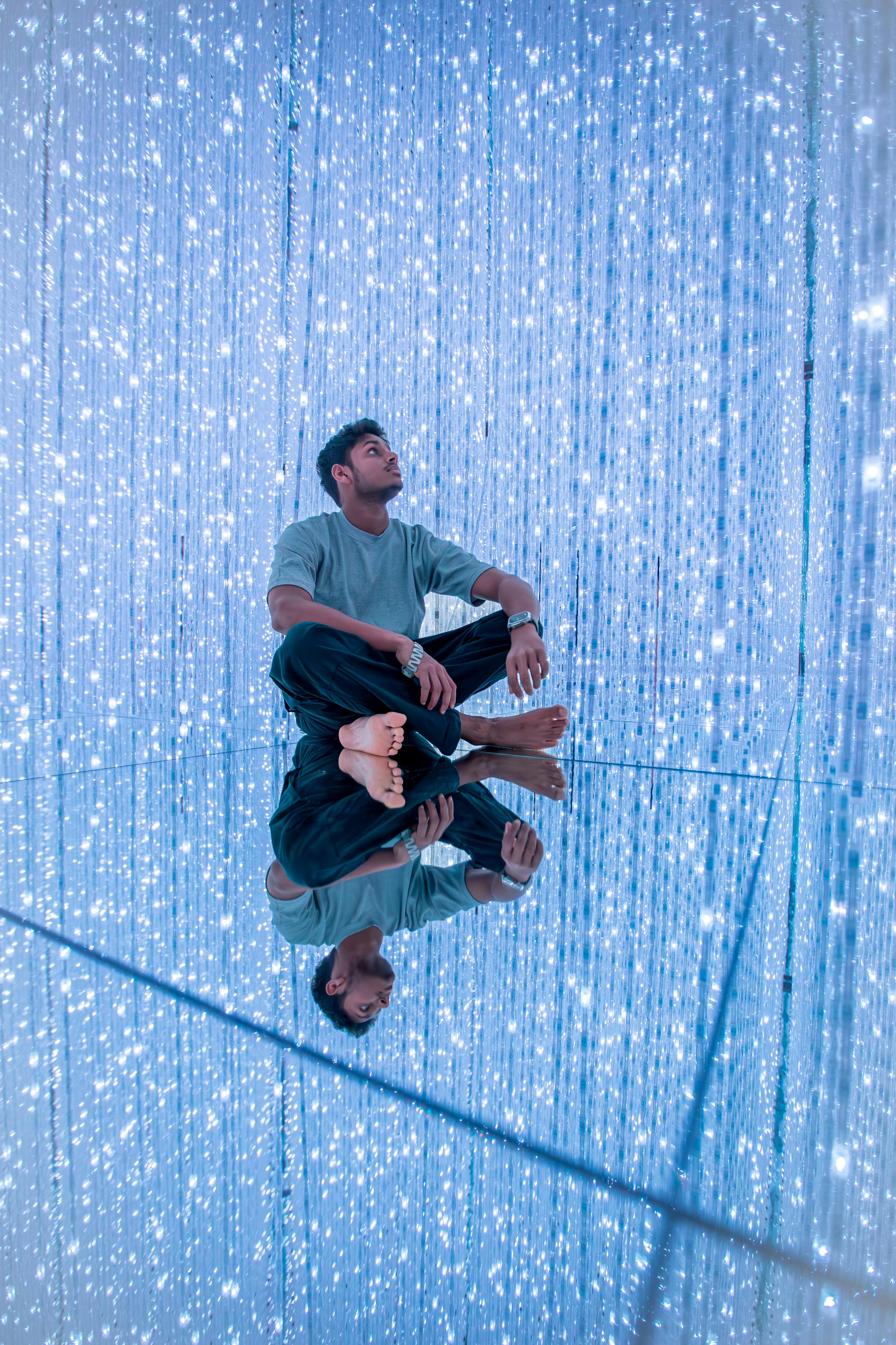 Man sitting barefoot in digital art exhibit with reflective floor