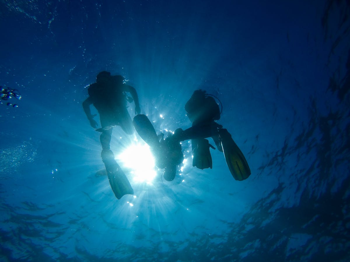 Silhouette of divers underwater with sun rays at Koh Tao