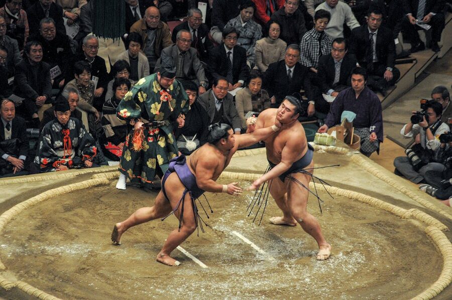 Two sumo wrestlers locked in combat during a traditional match with enthusiastic audience