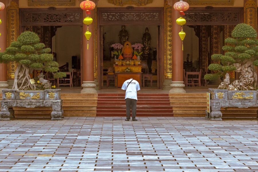 Person praying outside a temple adorned with colorful lanterns in Da Nang