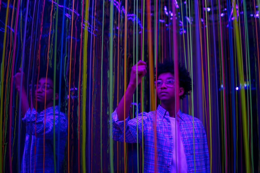 Young person interacting with colorful neon light strings in a reflective art installation