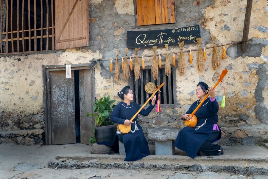 Women in traditional Vietnamese attire playing guitars in a rustic setting