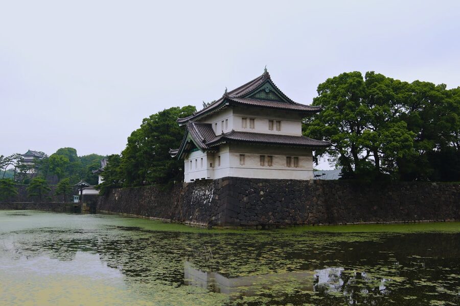 A historic watchtower structure at the Tokyo Imperial Palace next to a moat with tree-lined banks