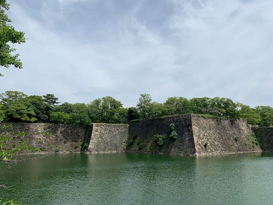 Scenic view of a castle moat surrounded by stone fortification walls and green trees in Japan
