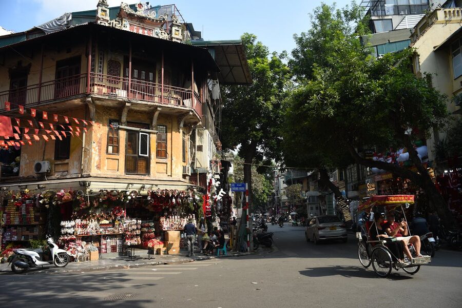 Traditional rickshaw and pedestrians on a street in Hanoi Old Quarter