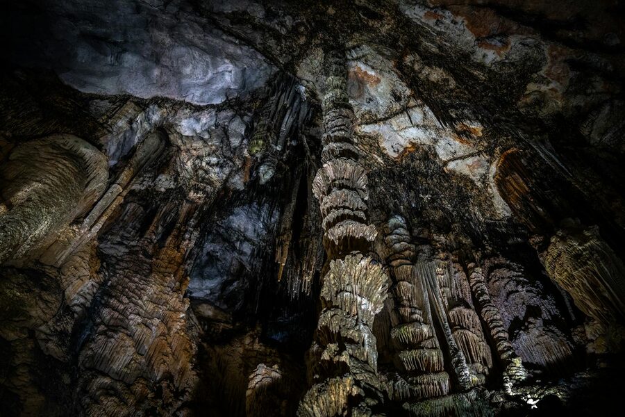 Vast cave chamber with glistening stalactites lit by torchlight