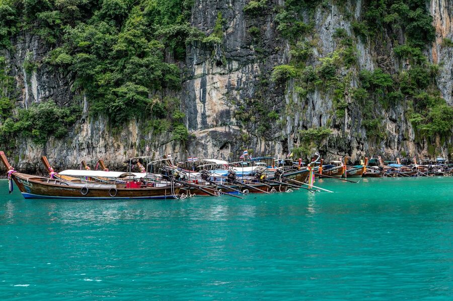 Traditional longtail boats moored near dramatic coastal cliffs in Phuket Thailand