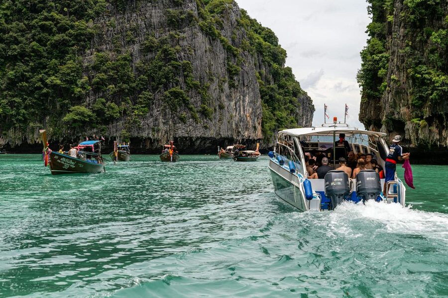 Tourists on a speedboat cruising past towering limestone cliffs in Phuket Thailand