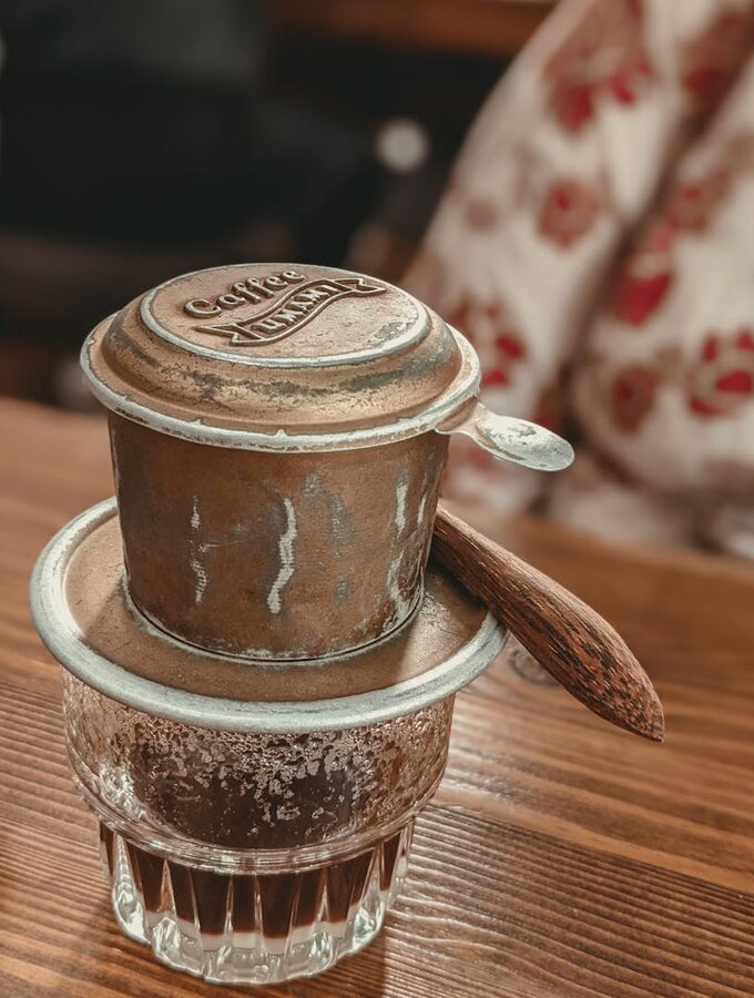 A phin filter dripping coffee slowly into a small glass on a wooden table