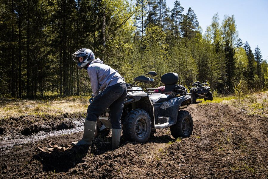 Person in helmet standing next to a quad bike covered in mud
