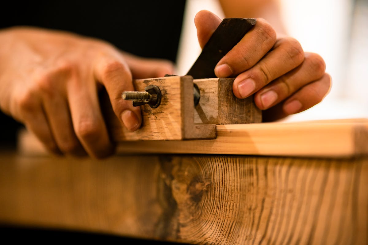 Hands meticulously adjusting a hand plane tool on a wooden plank at a workshop bench