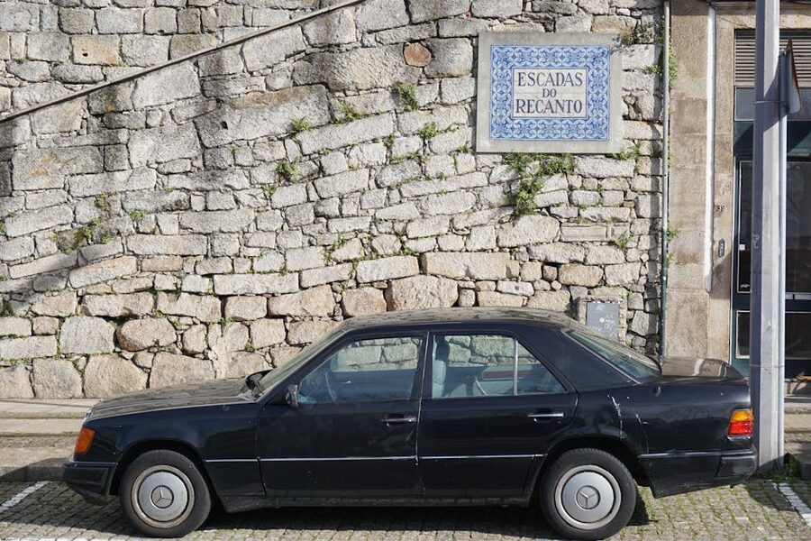 Vintage car parked by a tile wall with Portuguese signage in Porto
