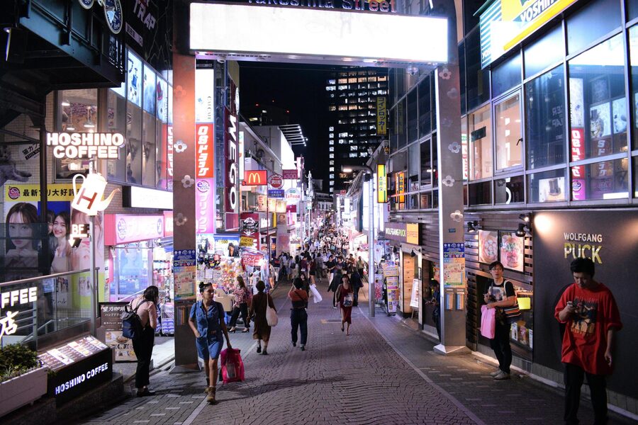 Brightly illuminated Takeshita Street in Harajuku Tokyo with neon signs and people shopping