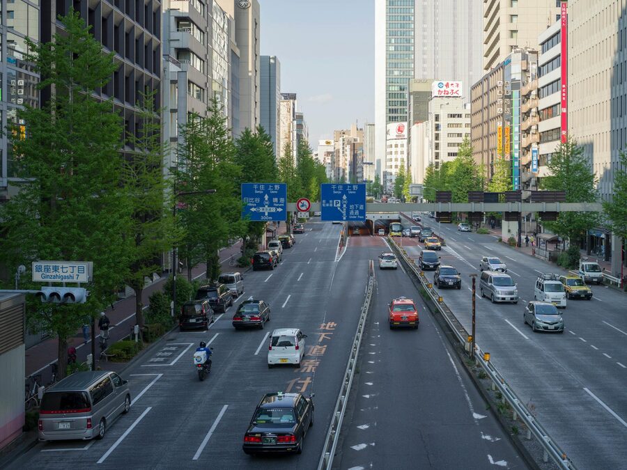 Daytime view of a wide Tokyo boulevard with cars, taxis, and tall buildings on both sides