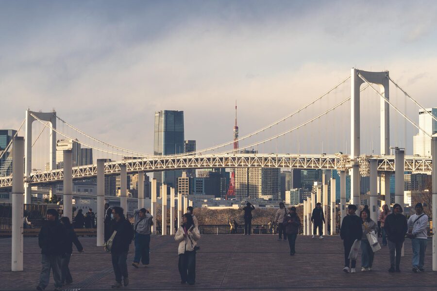 People walking along a waterfront path at sunset with Rainbow Bridge and Tokyo skyline in background