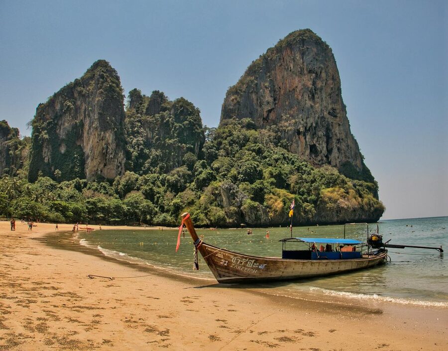A longtail boat docked on the shore at Railay Beach with limestone cliffs behind