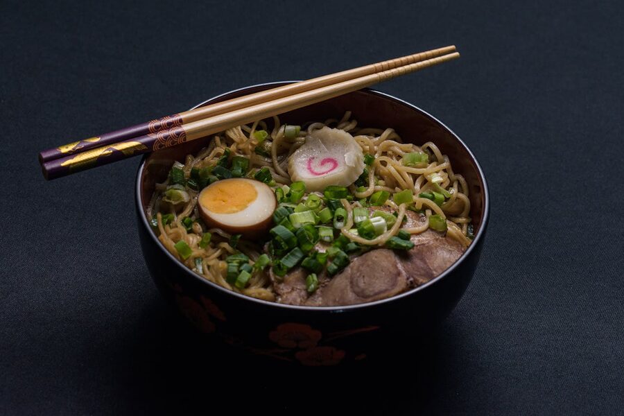 Japanese ramen with egg and scallions topped with chopsticks