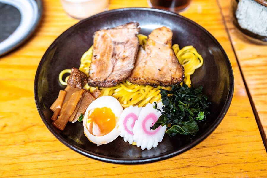 Black bowl of ramen with sliced chashu pork, a halved egg, and toppings served on a wooden table