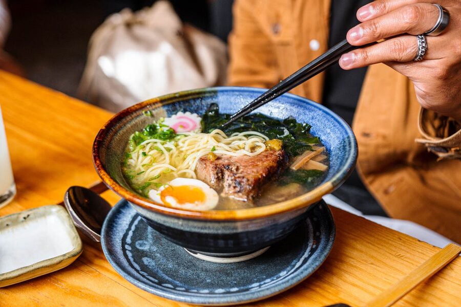 A bowl of ramen with chopsticks lifting noodles, showing a mix of toppings and rich broth