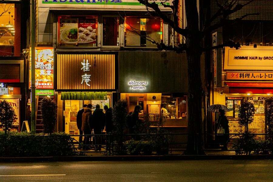 Street with illuminated ramen shops and patrons dining at night in Tokyo