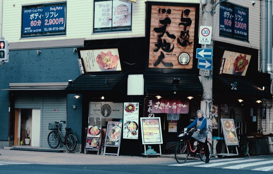 A Japanese restaurant storefront on an urban street with a cyclist passing by
