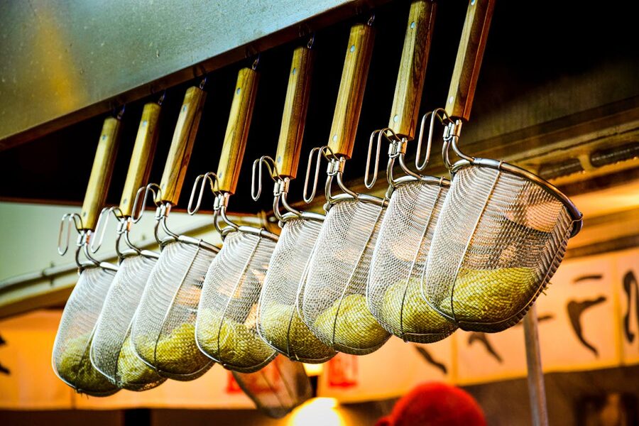 Metal noodle strainers hanging in a row inside a Japanese ramen restaurant kitchen