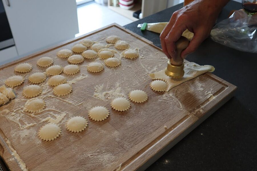 Fresh ravioli being cut with a pasta cutter on a floured board
