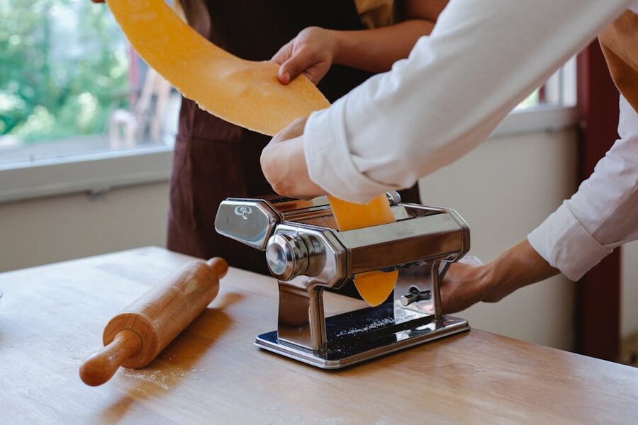 Hands feeding pasta dough through a hand-cranked pasta maker