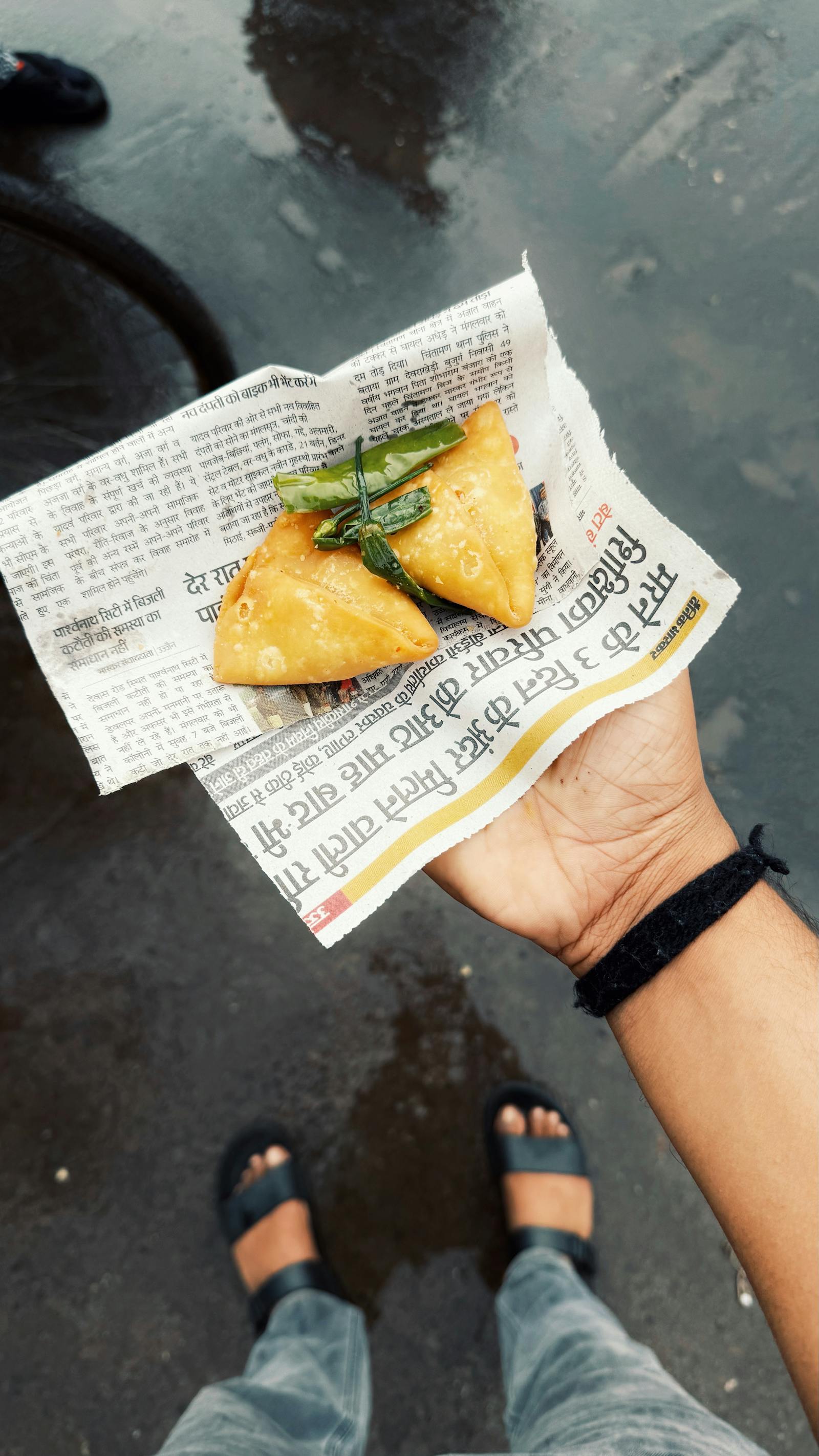 Freshly fried samosas wrapped in newspaper, held in a hand