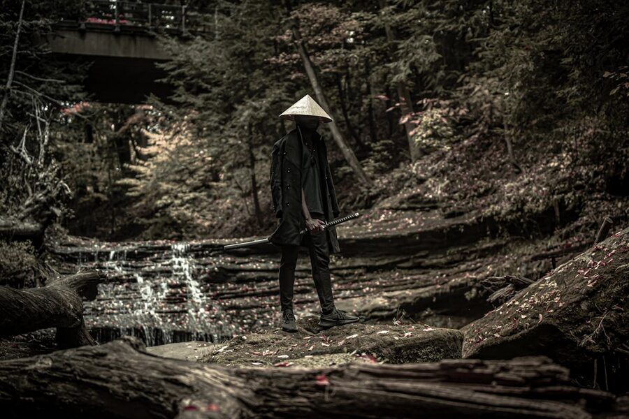 Lone figure in traditional samurai outfit standing in a forest holding a sword