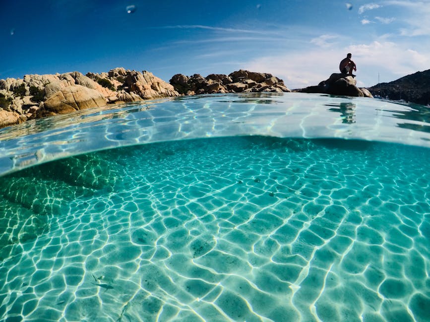 Person sitting on rocks beside extremely clear water at La Maddalena
