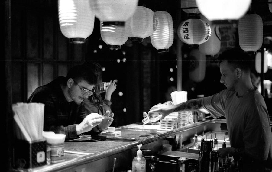 Bartender pouring spirits at a lantern-lit Japanese bar counter