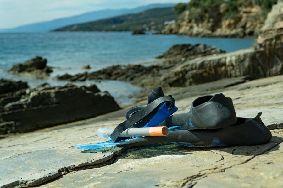 Snorkeling fins and mask resting on light sand near the waterline of a Bali beach